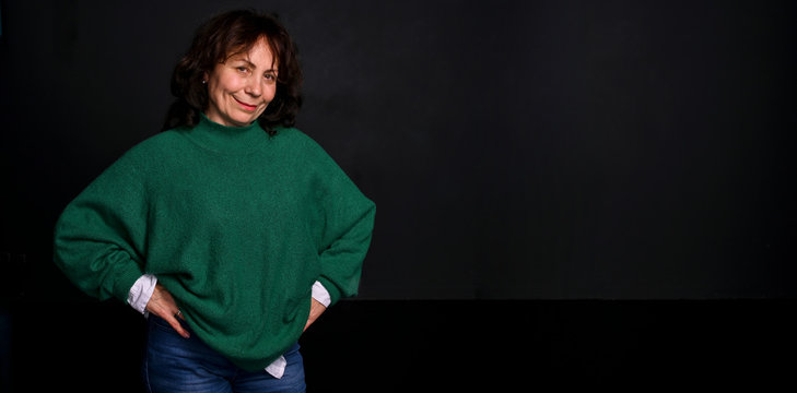 Woman age model. Beautiful adult woman in a green sweater on a black background. Filming in the studio. Banner, long format. Copy space