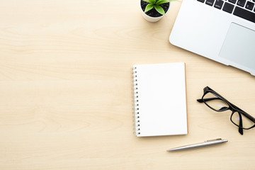 Wood office desk table with blank notebook page with pen, laptop computer and supplies. Top view with copy space, flat lay.