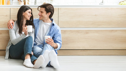 Obraz premium Young couple enjoying coffee, sitting on floor at kitchen
