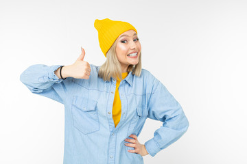 blond girl in a stylish denim shirt and yellow hat shows like on a white studio background