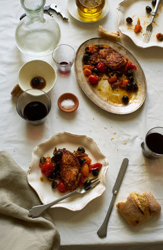Overhead image of family dinner table with roasted fish, tomatoes, olives and wine