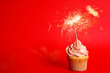 Birthday cupcake with sparkler on red background. Space for text