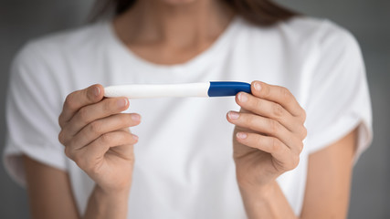 Close up focus on pregnancy test in female hands of future mother. Young woman holding plastic stick, waiting for good results after infertility treatment, maternity fertility check concept.