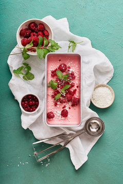 Pink ice cream with raspberries and red currants on green background. Top view