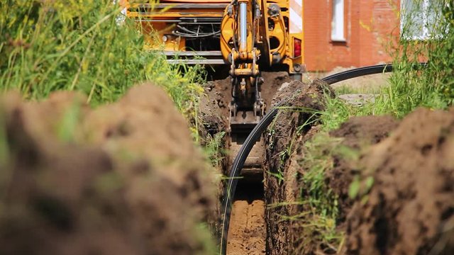 An excavator digs a trench for laying a cable. Summer sunny day. Excavator digs a trench for laying the cable