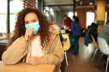 African-American woman with disposable mask in cafe. Virus protection