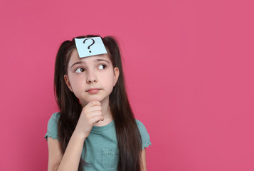 Pensive girl with question mark sticker on forehead against pink background. Space for text