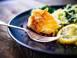 Risotto with fried cod on wooden background