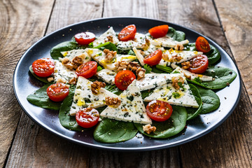 Fresh salad - blue cheese, cherry tomatoes, spinach, walnuts on wooden background