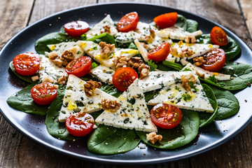 Fresh salad - blue cheese, cherry tomatoes, spinach, walnuts on wooden background