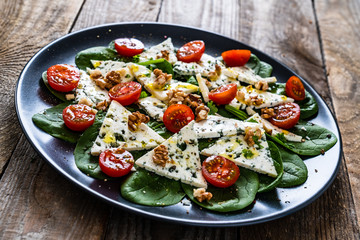 Fresh salad - blue cheese, cherry tomatoes, spinach, walnuts on wooden background