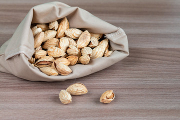 Unpeeled raw almonds in a handmade textile bag, organic and healthy food concept. Space for text, wooden table 