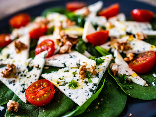 Fresh salad - blue cheese, cherry tomatoes, spinach, walnuts on wooden background
