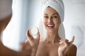 Cheerful young female blogger demonstrating organic cream, applying it on skin after showering in...