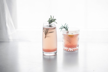 Pink grapefruit drink in two decorative glasses on a white background, garnished with rosemary.