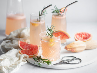 3 glasses of grapefruit cocktail on a marble tray with rosemary and grapefruit slices, pitcher and mousseline napkin
