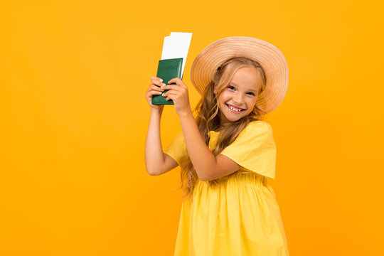 Beautiful girl with long hair holds a passport with tickets and smiles, picture isolated on yellow background