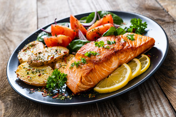 Fried salmon steak with potatoes and vegetables on wooden table