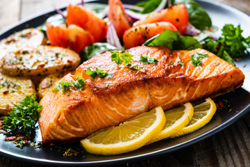 Fried salmon steak with potatoes and vegetables on wooden table