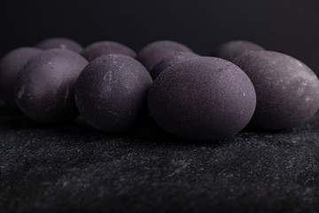 Close-up dark easter eggs on stone table with black backdrop. Colored with wine.
