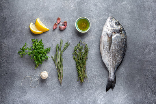 Flat lay with fish dorada or sea bream, herbs, lemon and oil
