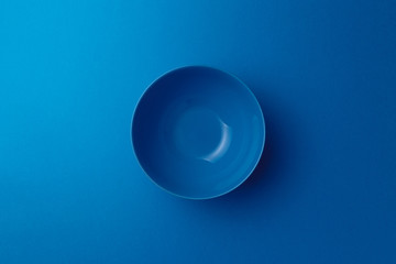 Empty ceramic blue round plate on classic blue background. Top view. Flat lay. Copy space. Minimal creative concept. Trendy color