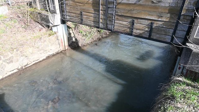 Bach flie&szlig;t unter einem weit ge&ouml;ffneten rustikalen schleusentor hindurch