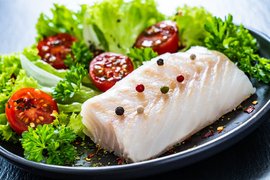 Fresh raw cod with vegetables on black stone board