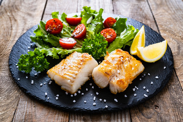 Fish dish - fried cod fillet with vegetables on wooden table
