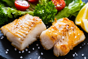 Fish dish - fried cod fillet with vegetables on wooden table