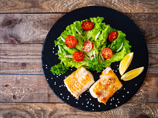 Fish dish - fried cod fillet with vegetables on wooden table