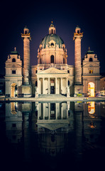 Fototapeta na wymiar Vertical image of Karslkirche church buiding and its reflectios at night time with tourists sitting nearby. Toruism and historical buildings in Viena. Asutria.