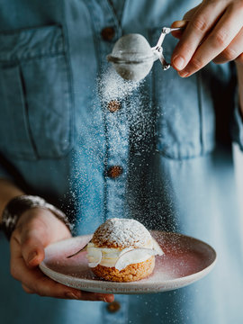 Woman sprinkles icing sugar on Choux cake with fresh berries