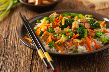Tofu with rice and vegetables. Served on brown plate.