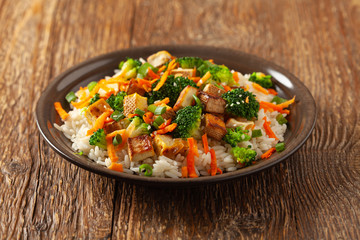 Tofu with rice and vegetables. Served on brown plate.