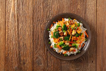 Tofu with rice and vegetables. Served on brown plate with chopsticks. Top view.