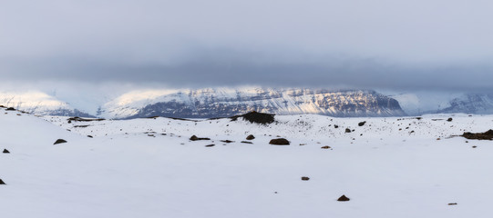 Isolated wintery Icelandic landscape in winter, with mountains in the background with light passing through the clouds in a wide landscape full of snow