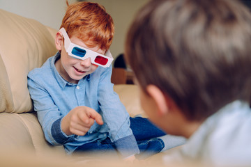 Portrait of a little boy pointing out to his brother an educational three dimension book. Cheerful kid playing with three dimensional glasses and interactive cinema at home. Leisure and movies
