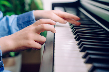 Obraz premium Unrecognizable child playing the piano. Detail of little boy hands touching a keyboard at home. Student of pianist musician rehearsing classical music. Educational music lifestyle.