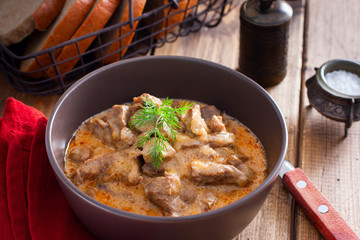 Traditional beef stroganoff in a ceramic bowl on a wooden table, selective focus