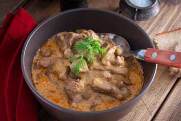 Traditional beef stroganoff in a ceramic bowl on a wooden table, selective focus