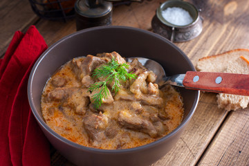 Traditional beef stroganoff in a ceramic bowl on a wooden table, selective focus