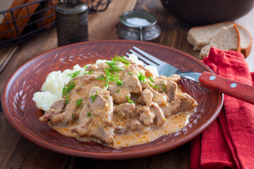 Traditional beef stroganoff in a ceramic bowl with mashed potato on a wooden table, selective focus