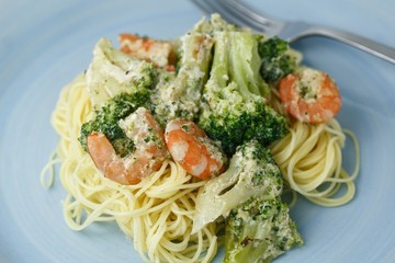 Creamy pasta with broccoli and shrimp on a blue plate with a fork