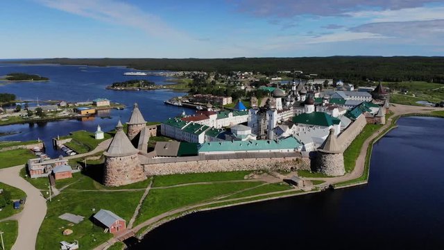 Smooth cinematic flyby of the Solovetsky monastery from the side of the Holy Lake with a view of the White Sea on a clear sunny day. Solovetsky monastery is an old (1420) ROC monastery.