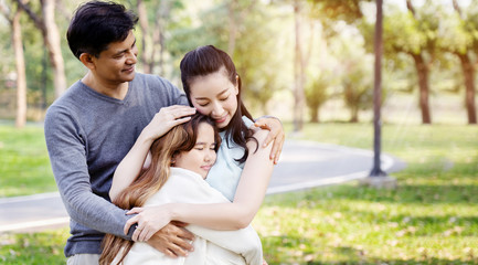 Asian family has Father and mother hugging their daughters, standing happy with a smile in the park.