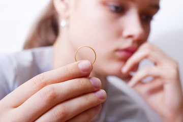 A beautiful girl with a sad face holds a gold wedding ring. The doubting bride. The concept of the...