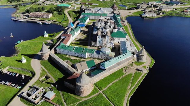 Smooth cinematic flyby of the Solovetsky monastery from the south side with a view of the White sea, Saint Lake and nearby village on a clear sunny day with contrast lighting.