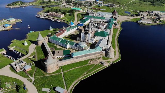Smooth cinematic flyby of the Solovetsky monastery from the south side with a view of the White sea, Saint Lake and nearby village on a clear sunny day with contrast lighting.