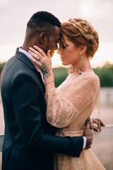 An African man and a Caucasian woman romantically touch each other in the sunset light. Close-up...